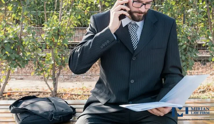 A man, likely a lawyer is sitting on a bench outdoors.